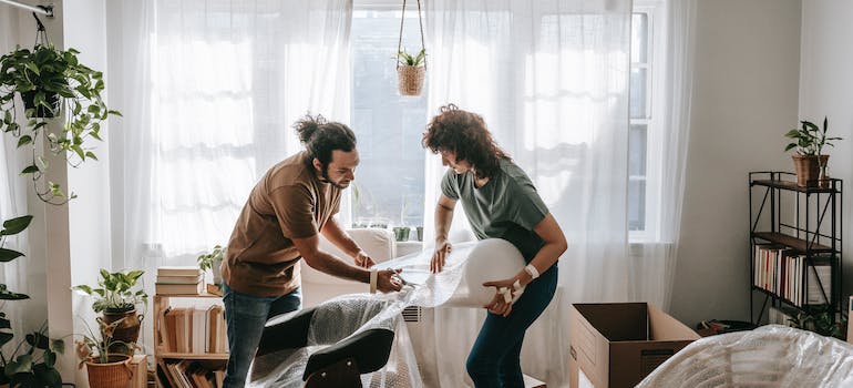 Two people following ultimate winter moving tips and wrapping furniture in plastic.